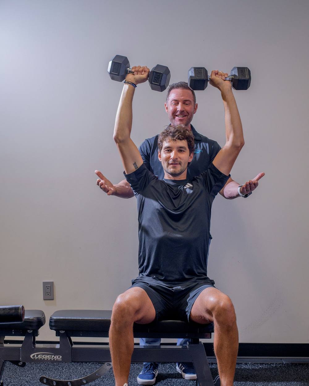 Bryan Greene spotting a client’s dumbbell overhead press